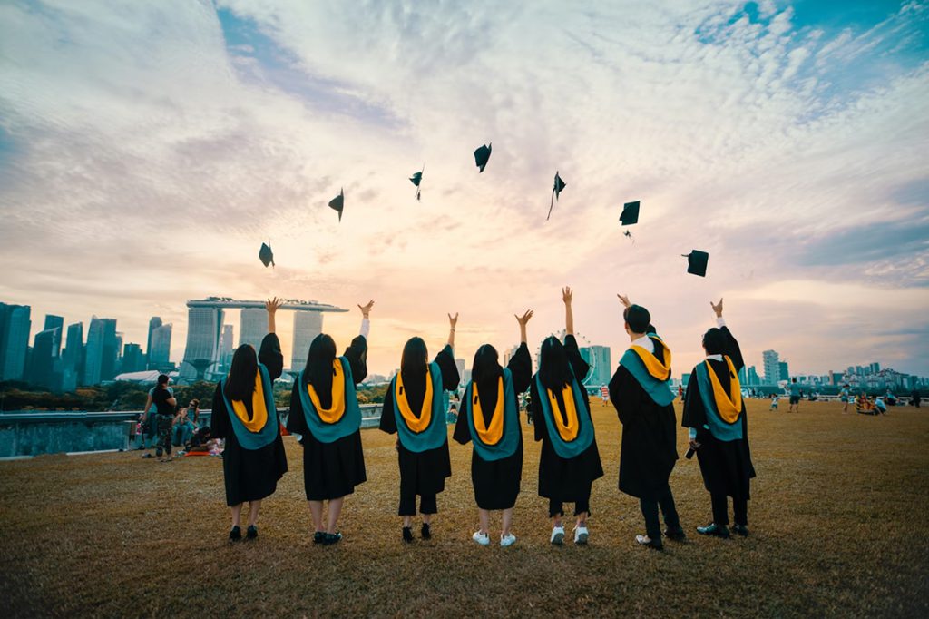 Graduates in academic gowns celebrating outdoors as caps are thrown into the air.
